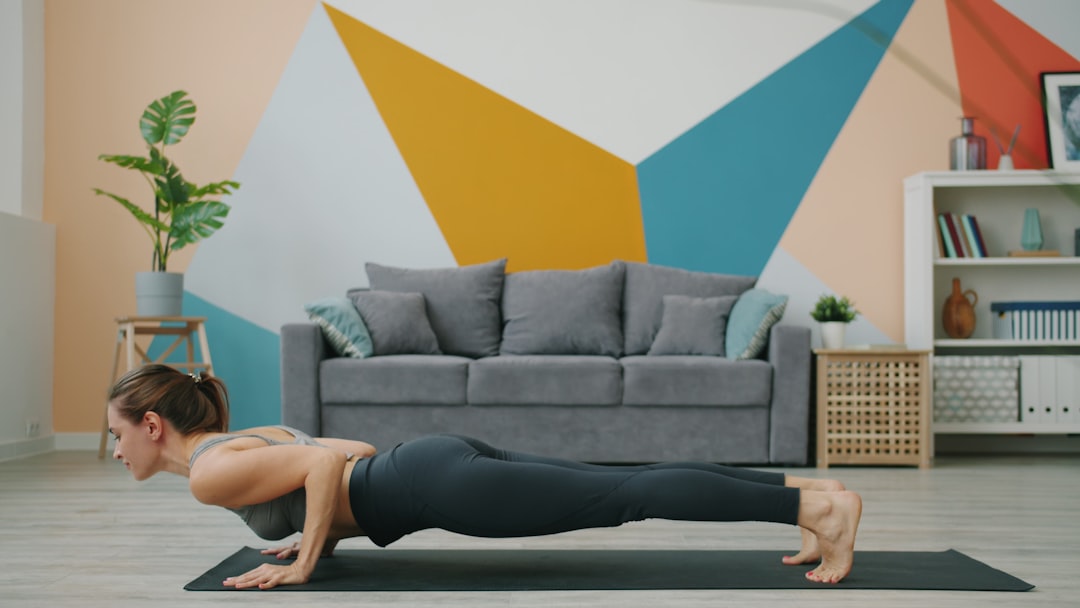 Woman doing yoga following online class on TV - Athletic young lady is exercising at home in plank position then doing yoga downward dog asana stretching body on mat. Millennials and sports concept.