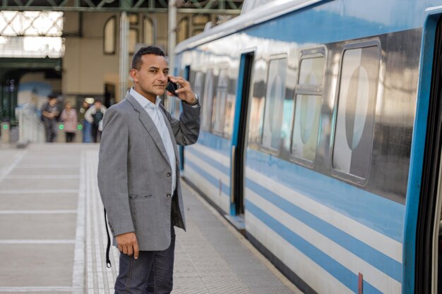 person talking into phone train station - Young latin man talking on a mobile phone on the platform of a ...